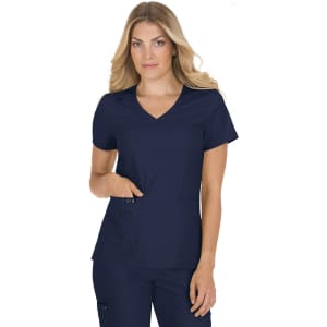 A woman wearing a navy blue medical scrub top with a V-neck and two front pockets. The top has a branding logo.