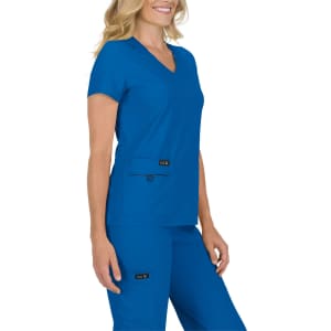 A woman wearing a blue scrub top with a v-neckline, paired with matching blue scrub pants. The outfit features pockets.