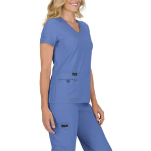 A woman wearing a short-sleeved, blue scrub top with two front pockets. The outfit includes matching blue pants.