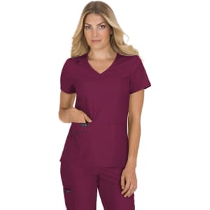 A woman is wearing a burgundy scrub top with a v-neck and pockets. The top features a logo.