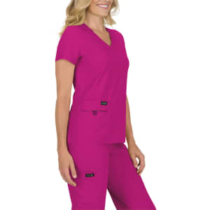 A woman wearing a vibrant fuchsia scrub top and matching pants, featuring pockets and branding.