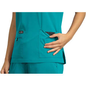 A teal top featuring pockets, with a patterned fabric visible from one pocket. The garment has a logo tag.