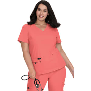 A model wearing a coral scrub top with a V-neck and two front pockets, holding a stethoscope.