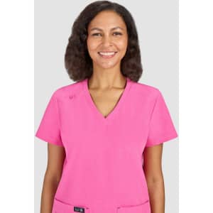 A woman smiles while wearing a bright pink scrub top. The top has short sleeves and a v-neck design.