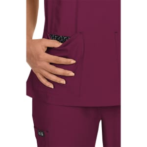 A scrub top in a rich burgundy colour with polka dot pockets, featuring a hand placed in one pocket.