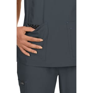 A grey medical top with two front pockets, displaying a polka dot lining and a hand placed in one pocket.