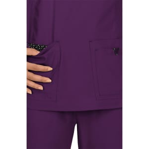 A purple scrub top featuring pocket details with a polka dot pattern. The fabric is smooth and lightweight.