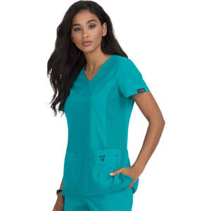 A scrub top in teal, featuring a V-neck and two front pockets, modelled by a woman with long dark hair.
