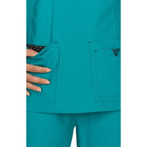 A teal scrub top featuring two front pockets, with a polka dot lining visible in one pocket.