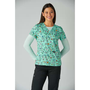 A floral print scrubs top in mint green, featuring a variety of colourful designs, worn over a light blue long-sleeve shirt.