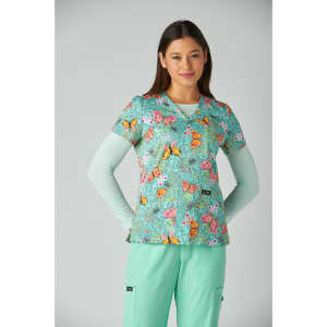 A woman models the Leslie Top in a vibrant print featuring butterflies, with a mint green background and matching trousers.