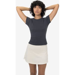 A fitted cap sleeve baby tee in dark grey, paired with a light-coloured skirt. The model has curly hair and a neutral background.