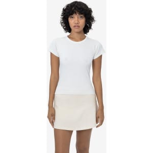 A woman wearing a white cap sleeve garment dye baby tee paired with a cream skirt, standing against a plain background.