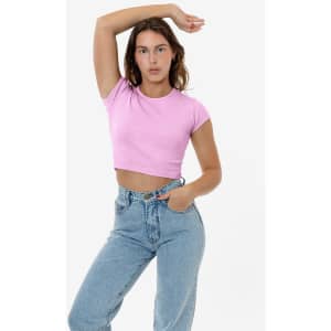 A pink cap sleeve crop top is styled with high-waisted light blue jeans, featuring a casual pose.