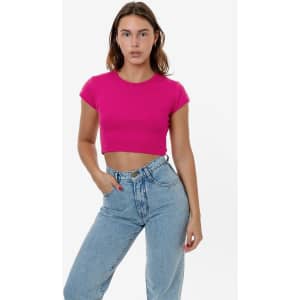 A pink cap sleeve crop top displayed on a model, paired with light blue jeans. Features a logo on the garment.