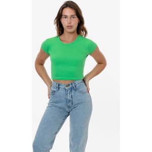 A woman stands confidently wearing a bright green cap sleeve crop top and light blue jeans. The top has a logo.