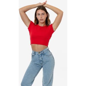 A model poses in a red cap sleeve crop top paired with light blue jeans. The top features a fitted design and has a logo.
