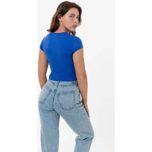 A woman stands facing away, wearing a blue cap sleeve crop top and light blue jeans. The top has a fitted style.