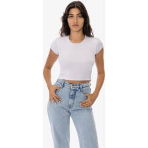 A woman models a light purple cap sleeve crop top paired with high-waisted blue jeans. The top features a minimal logo.