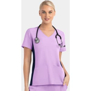 A mock wrap top in lilac with contrast navy panels, featuring short sleeves and pockets, worn by a model with a stethoscope.