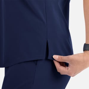 A navy blue women's V-neck top featuring a tuckable design and side slits. The image includes a hand holding the fabric.
