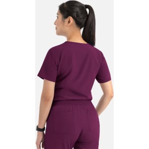 A woman wearing a purple women's tuckable V-neck top, viewed from the back, with a logo visible on the top.