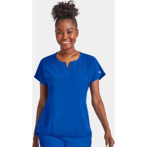 A woman wearing a bright blue notched neck dolman top, smiling confidently with a simple design and a logo.