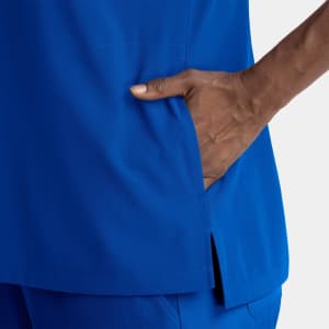 A women's dolman top in a vibrant blue, featuring a notched neck and side slits with a hand in the pocket.