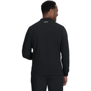 A man wearing a black jacket viewed from the back, featuring a simple design and a logo.