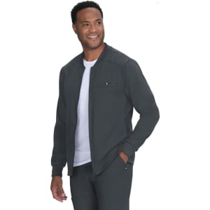 A man in a dark grey jacket with a zip, smiling and wearing a white t-shirt underneath. The jacket features a logo.