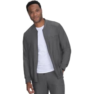 A man wears a grey jacket over a white shirt, featuring a zip pocket and a casual style. The jacket has a logo.