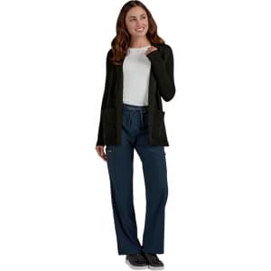 A woman in a black Kori Sweater with pockets, paired with navy trousers and a white top, smiling and pointing.
