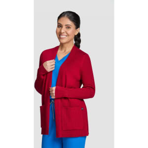 A red Kori Sweater featuring two front pockets, styled with a blue top, modelled by a smiling woman.