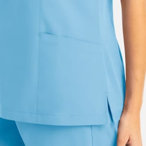 A light blue women's mock wrap top featuring a patch pocket and side slits. The top has a clean, modern design.
