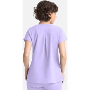 A lilac women's top featuring a back pleat and short sleeves, with a branding logo on it.
