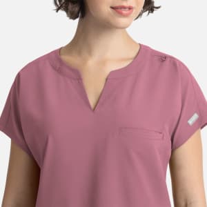 A close-up of a women's dolman top in mauve, featuring short sleeves and a single chest pocket. It has a logo.