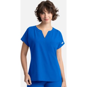 A woman wearing a bright blue dolman top featuring a v-neck and a single pocket. The top has rolled short sleeves.