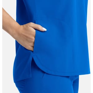 A bright blue women's top with three pockets, featuring a side slit and a relaxed fit. It has a logo on it.