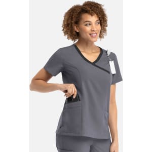 A woman in a grey mock wrap top with contrast trim, featuring a pocket. The top has a logo and a tag attached.