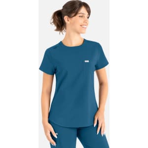 A woman wearing a teal round neck scrub top with a pocket and a logo, styled for uniforms.