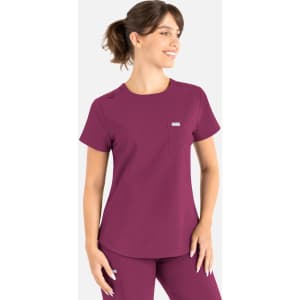 A scrub top in a rich plum colour with a pocket and branding, worn by a smiling model.