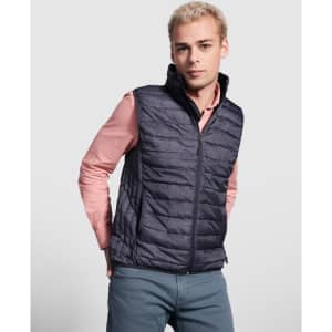 A man wearing a navy padded vest over a light pink shirt, standing against a grey background. The vest has a logo.