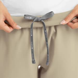 A pair of women's joggers in a light beige colour, featuring a grey drawstring waistband and a logo on the drawstring.