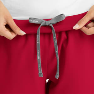 A pair of women's jogger pants in red, featuring a grey drawstring waist and a small logo on the drawstring.