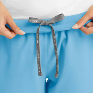 A pair of blue women's joggers featuring a grey tie at the waistband and a logo detail.