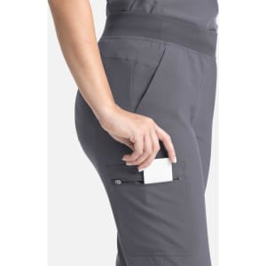 A pair of grey flare leg pants with a full elastic band, featuring a pocket on the side, showcasing a hand placing an item inside.