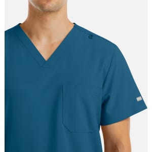 A men's v-neck top in teal with four pockets and a shoulder snap detail. Features branding on the sleeve.