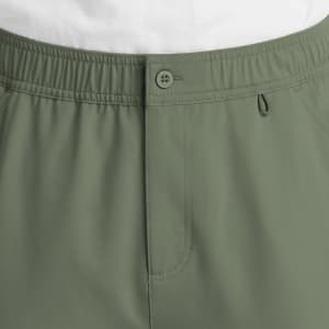 A close-up of olive green men's cargo pants featuring a fly front and button closure, with an elastic waistband.