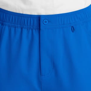 A close-up of blue cargo pants featuring a fly front, button closure, and elastic waistband, with a branding logo.