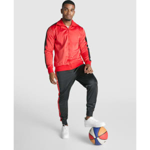 A track jacket in red with black accents, paired with matching black track pants. A basketball is on the ground.